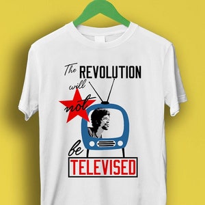 May include: White t-shirt featuring a blue and white television graphic and a red star. The text on the shirt reads "The Revolution will not be Televised".