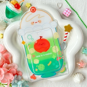 May include: Clear acrylic phone case with a cartoon melon design. The case features a gradient green and white background with a red melon character and the text "one in a melon". Additional decorative elements include a star-shaped spoon and a small cherry.
