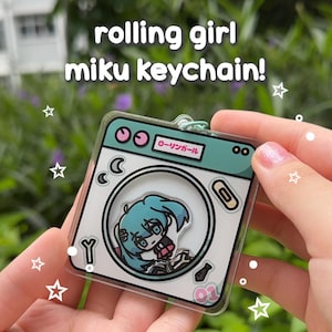May include: A clear acrylic keychain featuring a cartoon illustration of Hatsune Miku inside a washing machine. The keychain is blue, green, and white with the text "ローリングガール" in Japanese.