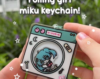 Op de afbeelding: Een transparante acryl sleutelhanger met een cartoonillustratie van Hatsune Miku in een wasmachine. De sleutelhanger is blauw, groen en wit met de tekst "ローリングガール" in het Japans.