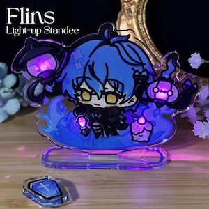 Puede incluir: Un expositor iluminado con un personaje de dibujos animados con pelo azul y ojos amarillos, sosteniendo una linterna. El expositor tiene un diseño de llama azul y está iluminado con luz púrpura. El texto "Flins Light-up Standee" está en la parte superior.