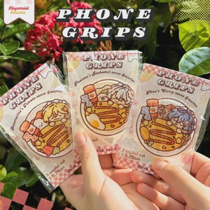 May include: Three phone grips in clear packaging, each featuring a cartoon illustration of a dish with a character. The packaging reads "PHONE GRIPS" and includes text like "Aventurine's Tomato Sauce Omurice." Each grip is approximately 2.26 inches.