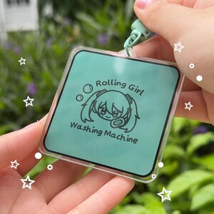 May include: A green and white keychain with a cartoon character and the text "Rolling Girl Washing Machine".