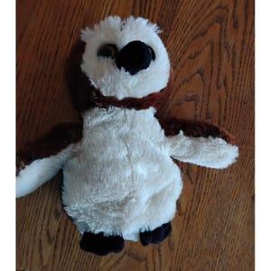 May include: A plush owl toy with a white body, brown wings and accents, and a black beak. The owl has large, round eyes and black feet. The toy is designed to resemble a real owl.