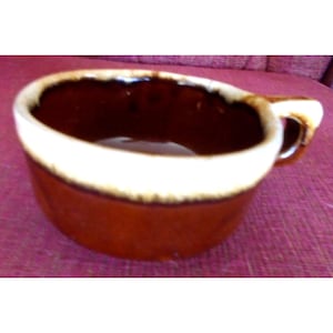 May include: A brown ceramic soup bowl with a white rim and a handle. The bowl has a glossy finish and a classic design, suitable for serving soups, stews, or other warm dishes. The handle provides a comfortable grip.