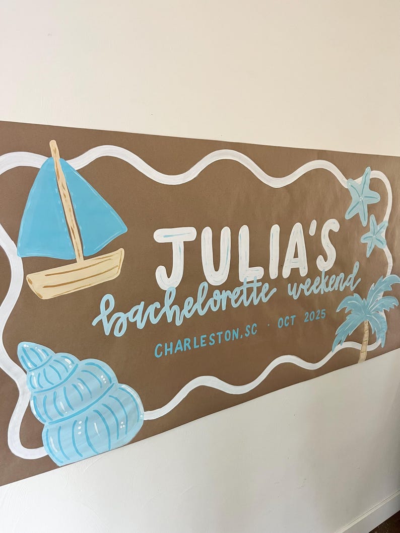May include: A brown paper banner featuring white wavy borders and hand-painted illustrations including a blue sailboat, a seashell, two starfish, and a palm tree. The text reads JULIA'S bachelorette weekend, CHARLESTON, SC - OCT 2025 in white and blue.