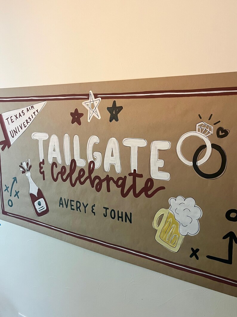 May include: A large brown paper banner featuring the hand-painted text Tailgate & Celebrate and Avery & John. Illustrations include a Texas A&M University pennant, stars, two interlocking rings, a champagne bottle, and a mug of beer with foam.