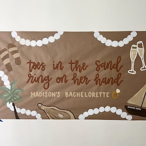 May include: A brown rectangular banner featuring white pearl-like beads, brown sandals, two champagne flutes, a palm tree, an oyster, and a sailboat. The text reads: toes in the sand ring on her hand MADISON'S BACHELORETTE with a ring icon.
