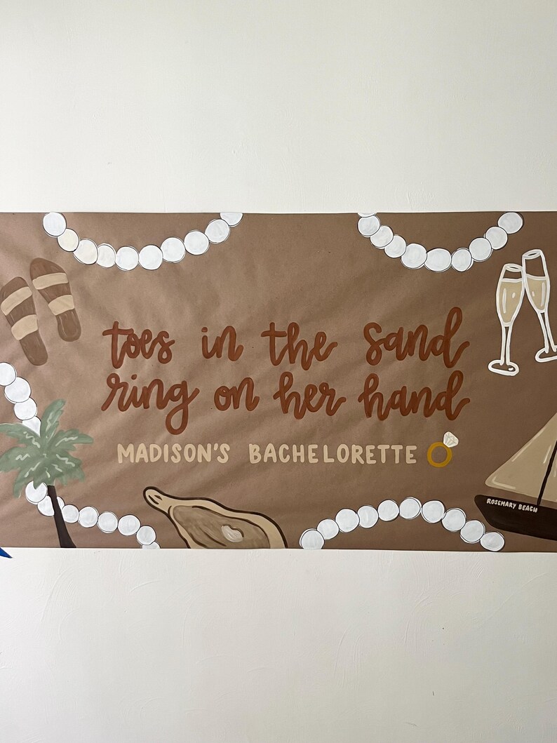 May include: A brown rectangular banner featuring white pearl-like beads, brown sandals, two champagne flutes, a palm tree, an oyster, and a sailboat. The text reads: toes in the sand ring on her hand MADISON'S BACHELORETTE with a ring icon.