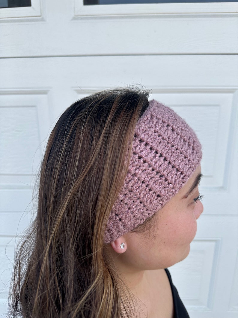 May include: A pink crocheted headband with a textured pattern. The headband is worn on a person's head.