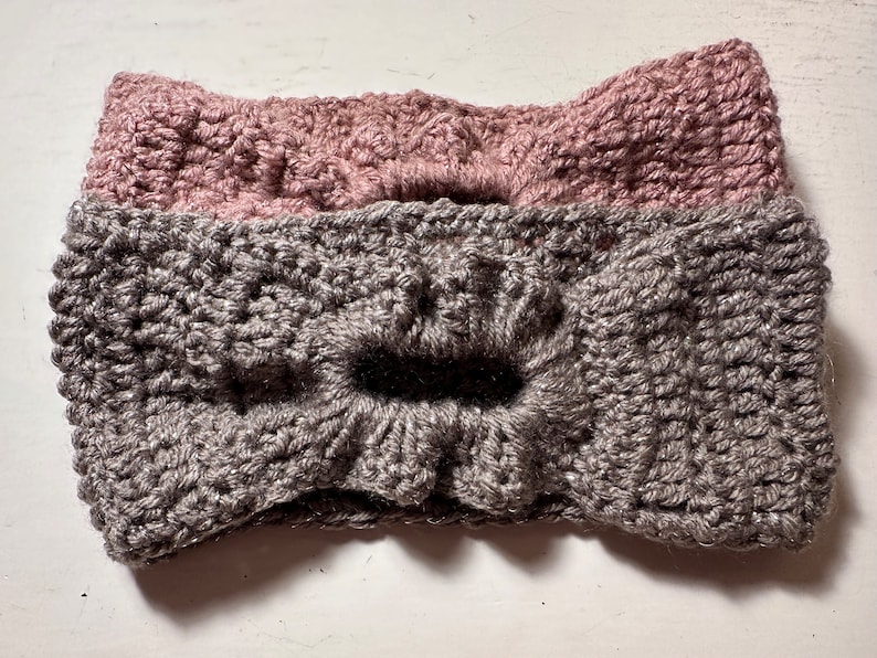 May include: Two crocheted headbands, one gray and one pink, with a bow detail.