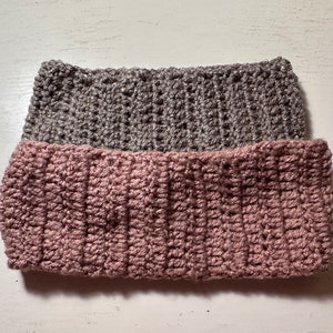 May include: Two crocheted headbands, one in a light pink color and the other in a gray color. The headbands are stacked on top of each other.