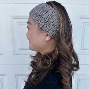 May include: A gray crochet headband with silver glitter thread. The headband is worn by a person with long brown hair.