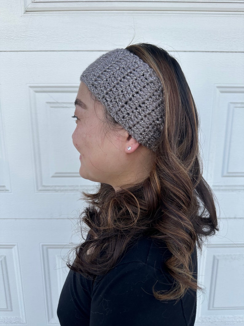 May include: A gray crochet headband with silver glitter thread. The headband is worn by a person with long brown hair.
