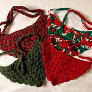 May include: Three crocheted neck warmers in red, green, and white. The red neck warmer has a scalloped edge. The green neck warmer has a scalloped edge. The white and green neck warmer has a geometric pattern.