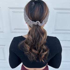 May include: A gray knitted headband worn by a person with long brown hair pulled back in a ponytail. The headband is tied in a knot at the back of the head.