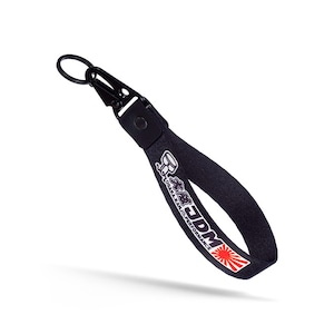 Può includere: Portachiavi nero con un logo JDM bianco e nero e una grafica di sole nascente rosso e bianco. Il portachiavi ha un cinturino nero e un anello metallico argentato.
