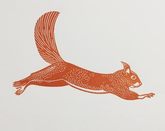 May include: A linocut print of a squirrel in mid-leap, rendered in shades of orange. The squirrel's body is detailed with small dots and lines, and its bushy tail curves upwards. The background is plain white.