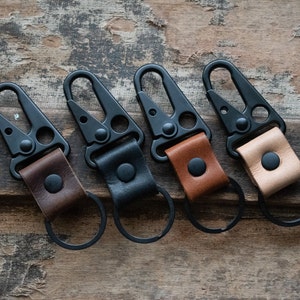 May include: Four black metal keychains with leather loops in brown, tan, and black. Each keychain has a metal ring and a clip.