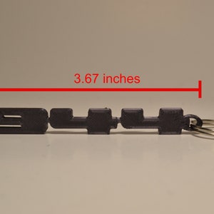 May include: A black 3D printed keyring with the text "911" and a silver key ring. The keyring is 9.3 cm long.