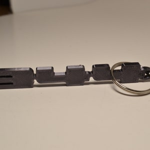 May include: A black plastic keyring with the word "SLUR" printed on it. The keyring has a silver metal ring.