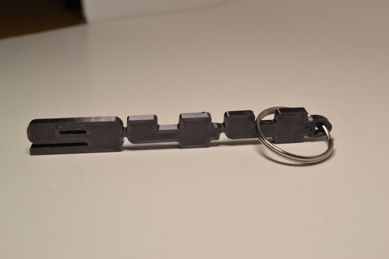 May include: A black plastic keyring with the word "SLUR" printed on it. The keyring has a silver metal ring.