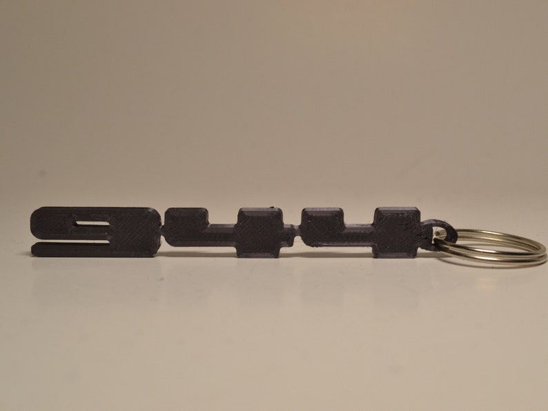 May include: A black 3D printed keyring with the number "3114" on it. The keyring has a silver metal ring.