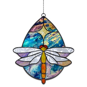 Peut inclure: Une décoration en verre coloré en forme de libellule sur fond bleu, jaune et violet. La libellule a une tête rouge et un corps jaune.