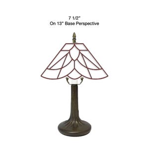 May include: A table lamp with a dark brown, textured tree-trunk base and a geometric stained glass shade featuring white panels outlined in dark red. The text 7 1/2" On 13" Base Perspective is displayed above the lamp, indicating its dimensions.