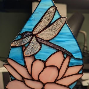 May include: A stained glass dragonfly with brown wings and a pink lotus flower on a blue background.