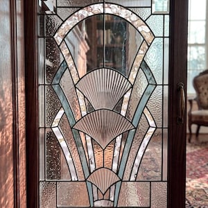 Pode incluir: Uma porta de armário retangular com moldura de madeira escura e um painel de vidro decorativo. O vidro apresenta um padrão geométrico em forma de leque, composto por segmentos de vidro transparente, texturizado e canelado, unidos por perfis metálicos escuros.