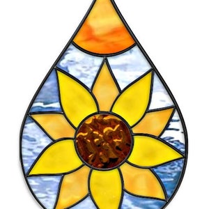 May include: A stained glass suncatcher in the shape of a teardrop with a yellow sunflower design and a blue and white background.