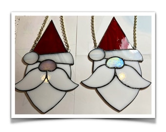 May include: Two stained glass Santa Claus ornaments. Each features a red hat, white beard, and a gold chain for hanging. The ornaments have a black outline and are designed with a festive holiday theme.