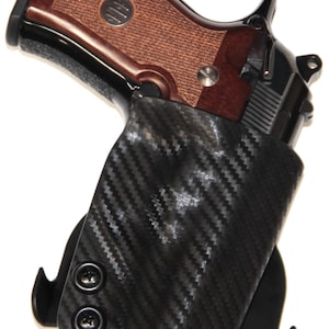 May include: A black carbon fiber holster with a black gun inside. The holster has two black screws and a black clip.