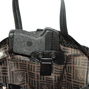 May include: A black handgun with a black holster is secured inside a brown handbag with a black handle. The holster has a black clip with the text "ULTI-CLIP" printed on it.