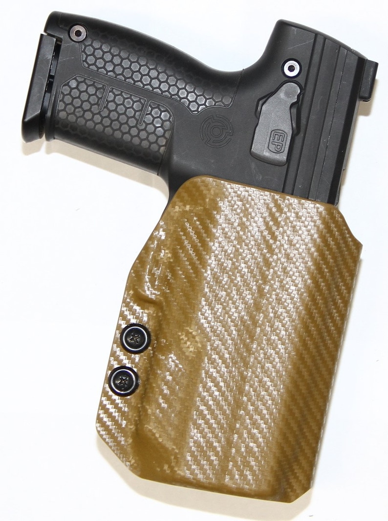 May include: A tan leather holster with a carbon fibre pattern and black snaps. The holster is designed to hold a handgun. The holster has a black plastic trigger guard.