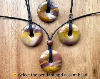 May include: Three round, yellow, brown, and purple stone pendants with a hole in the center, hanging from black cords with silver accent beads.  Select the pendant and accent bead.