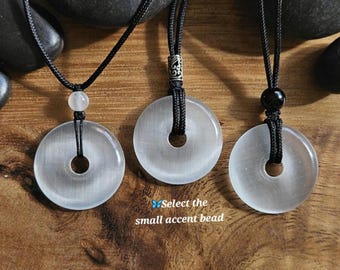 May include: Three necklaces with white moonstone pendants. Each pendant is a round disc with a hole in the center. The necklaces are on a wooden surface.  Select the small accent bead.