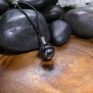 May include: A black gemstone pendant necklace with a silver clasp. The necklace is on a black cord and is resting on a wooden surface with black stones.
