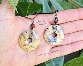 May include: Two stone pendants with a hole in the center, each suspended by a different type of rope. The pendants are beige, yellow, and gray. The text "Select the pendant & type of rope" is visible.