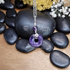 Könnte beinhalten: Ein kleiner 18 mm Amethyst-Donut-Pi-Stein-Anhänger an einer Silberkette. Der Anhänger ist mit Draht umwickelt und hat eine kleinere Amethystperle über dem Donutstein. Der Text im Bild lautet "Select a Chain or Rope".