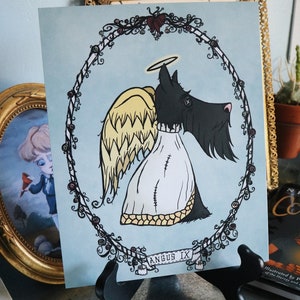 May include: A black and white illustration of a Scottish Terrier with angel wings and a halo. The dog is wearing a white robe with stitching. The illustration is framed with a black and white floral wreath and the text "ANGUS IX" is at the bottom.