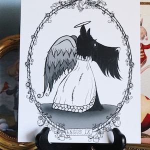 May include: Black and white illustration of a Scottish Terrier dog with angel wings and a halo. The dog is wearing a white robe with stitching. The illustration is framed with a decorative border of vines and flowers. The text "ANGUS IX" is written on a banner below the dog.