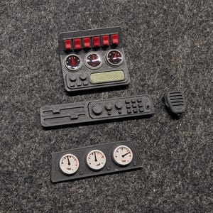 Könnte beinhalten: Eine Sammlung schwarzer 3D-gedruckter Modellkomponenten, darunter eine Schalttafel mit roten Schaltern und Messgeräten, eine Funktafel und ein Mikrofon. Enthält auch eine Tafel mit drei Temperaturanzeigen.