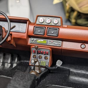 Op de afbeelding: Gedetailleerd model auto dashboard in bruin- en zwarttinten. Het dashboard heeft meters, ventilatieopeningen en een versnellingspook. Het stuur is zichtbaar aan de linkerkant. Het algehele ontwerp suggereert een vintage of klassieke auto.