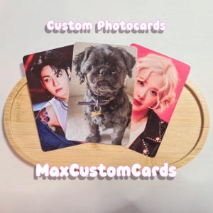May include: Three custom photo cards on a wooden tray. The cards feature images of a person, a dog, and another person. The text "Custom Photocards" and "MaxCustomCards" are displayed in a light purple font.