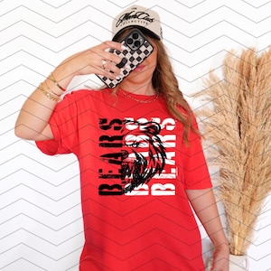 May include: A red t-shirt with the word "BEARS" in white and black text, along with a black and white graphic of a bear's head. The shirt is short-sleeved.