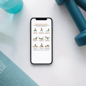 K&ouml;nnte beinhalten: Ein Smartphone zeigt eine Trainingsroutine "Inner Thigh Focus Set" mit &Uuml;bungsillustrationen. T&uuml;rkisfarbene Kurzhanteln und eine Wasserflasche umgeben das Telefon auf wei&szlig;em Untergrund, zur F&ouml;rderung von Fitness.
