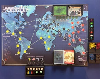 May include: A Pandemic board game set up with a world map, player pieces, and cards. The game board shows a world map with cities connected by lines. There are red, yellow, and black markers on the board. There are also cards and player pieces on the board.