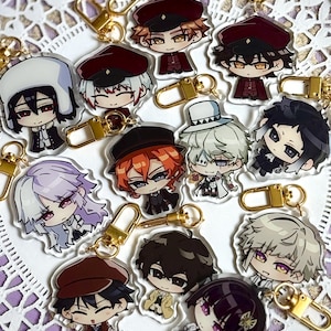 Può includere: Una collezione di dodici portachiavi in acrilico trasparente raffiguranti personaggi anime in stile chibi con diversi colori di capelli, abiti e cappelli. Ogni portachiavi è fissato a un moschettone in metallo color oro.
